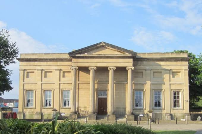 Front view of a classical-style building with tall columns and large windows, set against a blue sky.